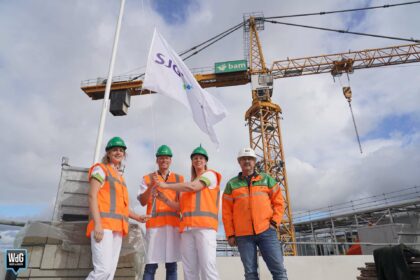 Drie SJG-medewerkers beklommen samen met BAM-hoofduitvoerder Manuel Habets de nieuwbouw om een SJG-vlag te hijsen